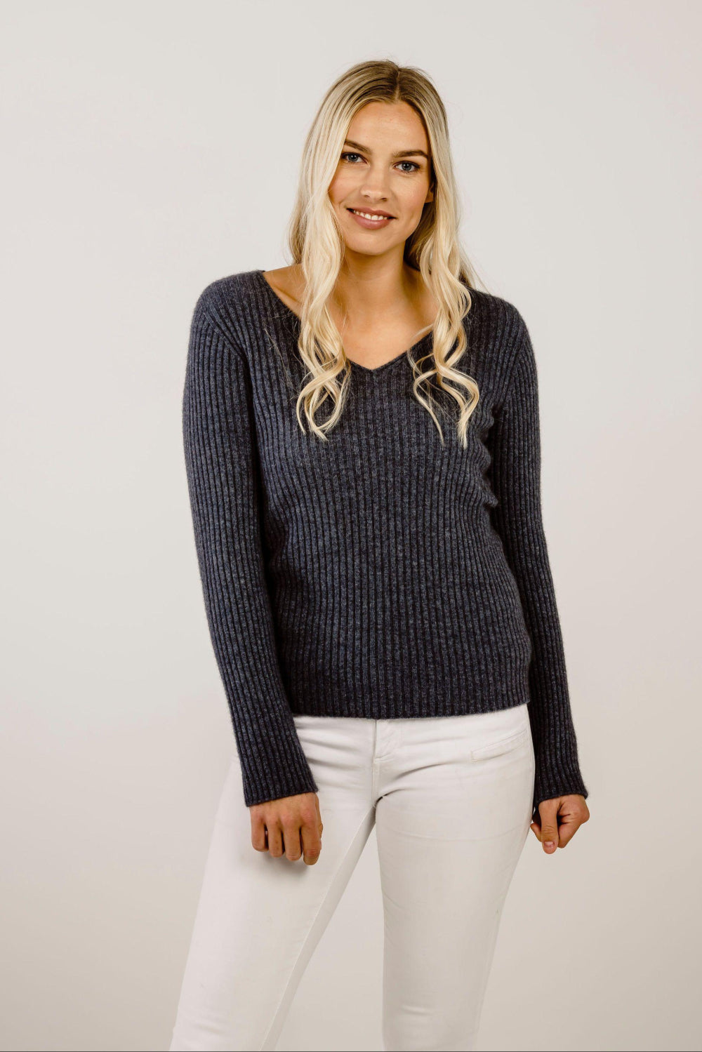 A woman wearing a dark ribbed sweater and white pants against a plain background