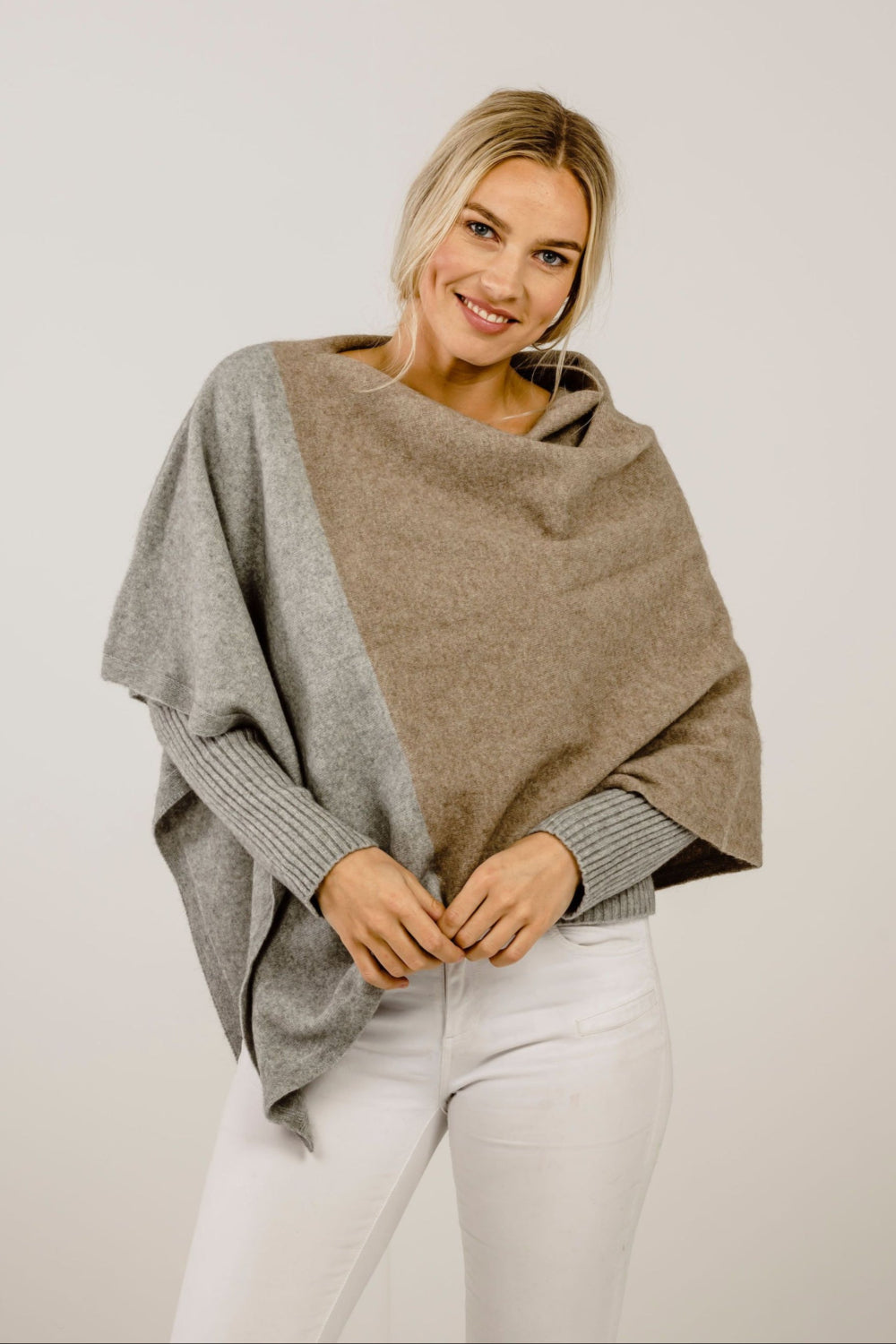 Woman wearing a two-tone poncho with gray and beige colors on a plain background