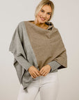 Woman wearing a two-tone poncho with gray and beige colors on a plain background