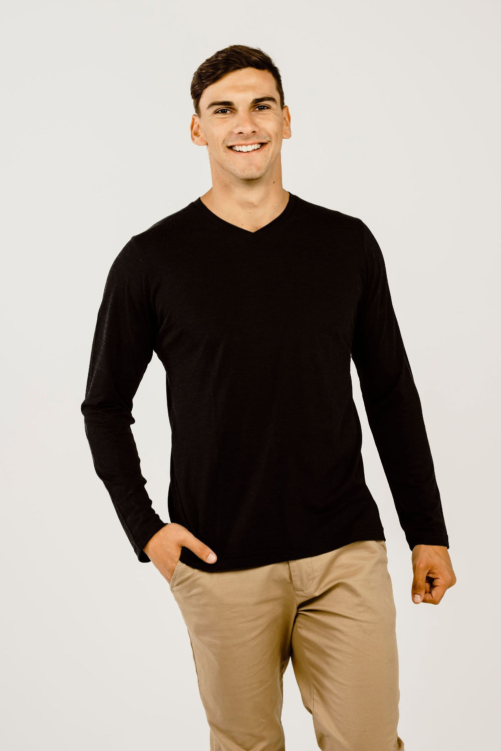 Man wearing a black long-sleeve shirt and beige pants on a white background