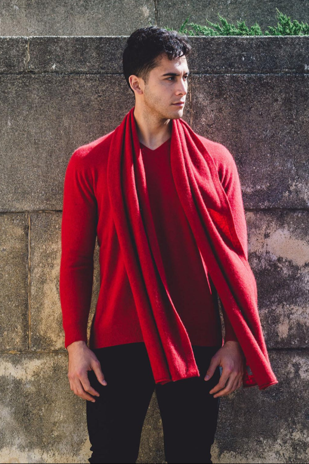 A man wearing a red Cashmere V Neck Sweater, standing next to a wall.